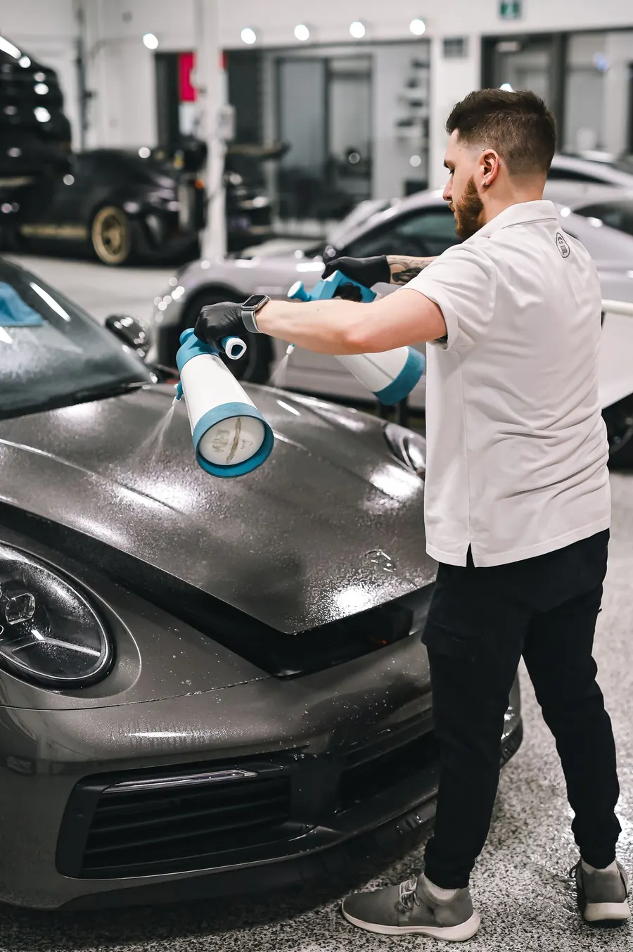 Detailer trägt eine Versiegelung mit der Sprühflasche auf eine graue Motorhaube auf